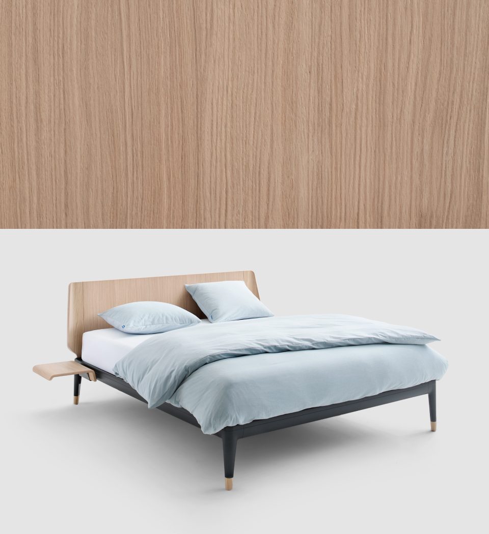 Auping Essential bed with an oak headboard and dark frame, next to an oak wood sample