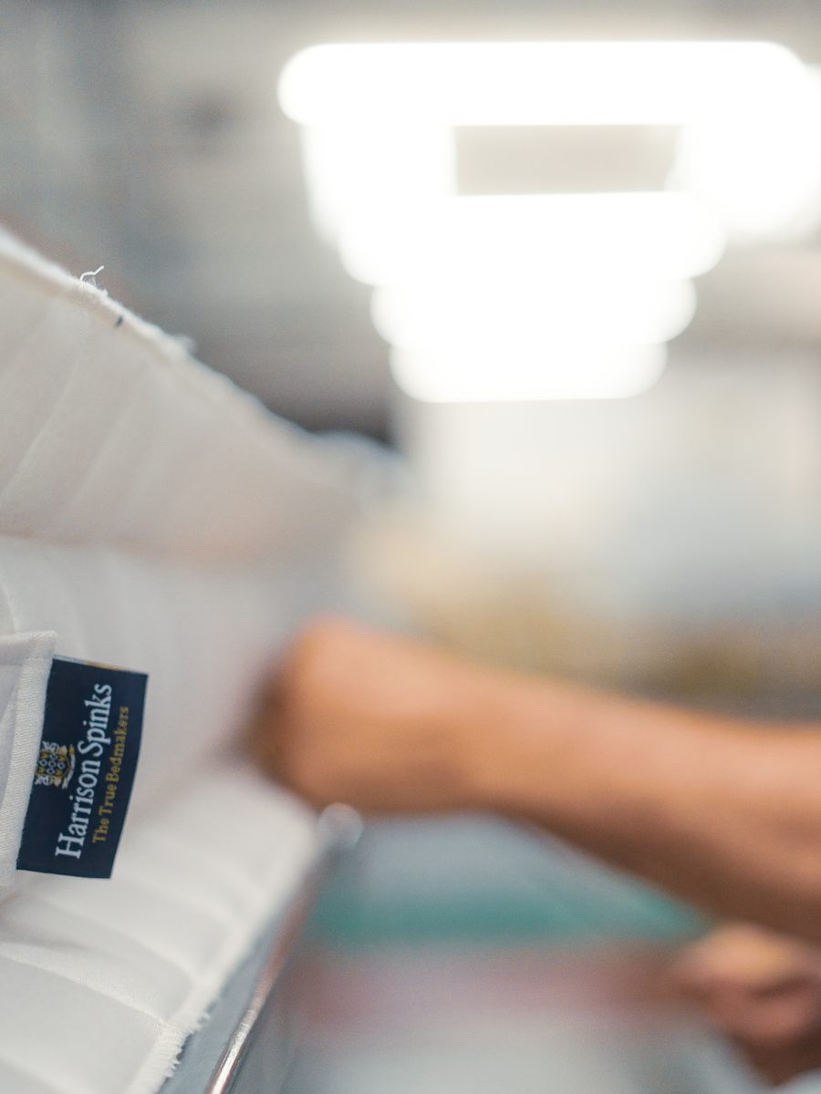 A craftsman hand-stitching the side of a Harrison Spinks mattress with its label